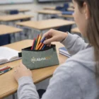 Student takes pens from a Rhys Tech Pouches case labeled Alphatech in class.
