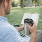 Man reading on a park bench, sipping coffee from a Fallon Double Wall Cup.