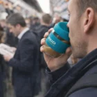 Man sipping coffee from a blue Reid Cups Tritan 230Ml cup on a crowded subway.
