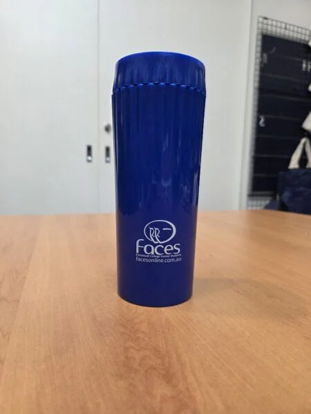 Blue plastic tumbler with Faces logo, perfect for reorder merchandise, on a wooden table indoors.
