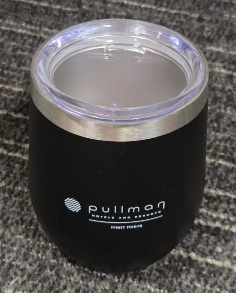 Black Pullman Hotels tumbler for those choosing between similar products; clear lid, gray surface.