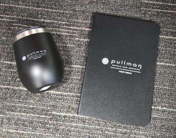 Black Pullman tumbler and notebook on a grey, striped carpet for product comparison.