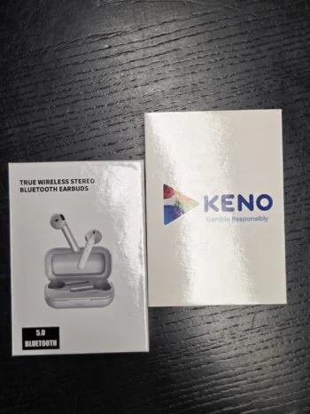 Box of wireless earbuds, perfect for event gifts, next to a Keno pamphlet on black surface.