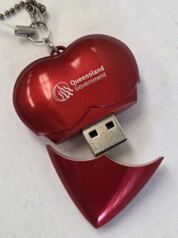 Red heart-shaped Cap USB Drive with Queensland Government logo on a white background.