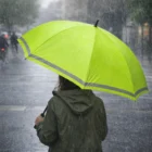 Person holding a bright green Sasha Umbrellas Safety umbrella in the rain on a city street.