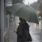 A person with a Kieran Umbrella waits at a rainy city bus stop.