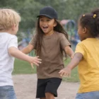 Three kids in Kids Staple Tees smiling and running toward each other outdoors.