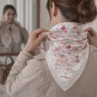 Woman ties a Celeste Fine-Silk Scarf around her neck, admiring herself in the mirror.