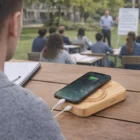A phone charges on a Bamboo Solar Power Bank at an outdoor class with people nearby.