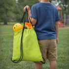 Child holding a green Soft Drawstring Go Bag with toys, standing near a playground.