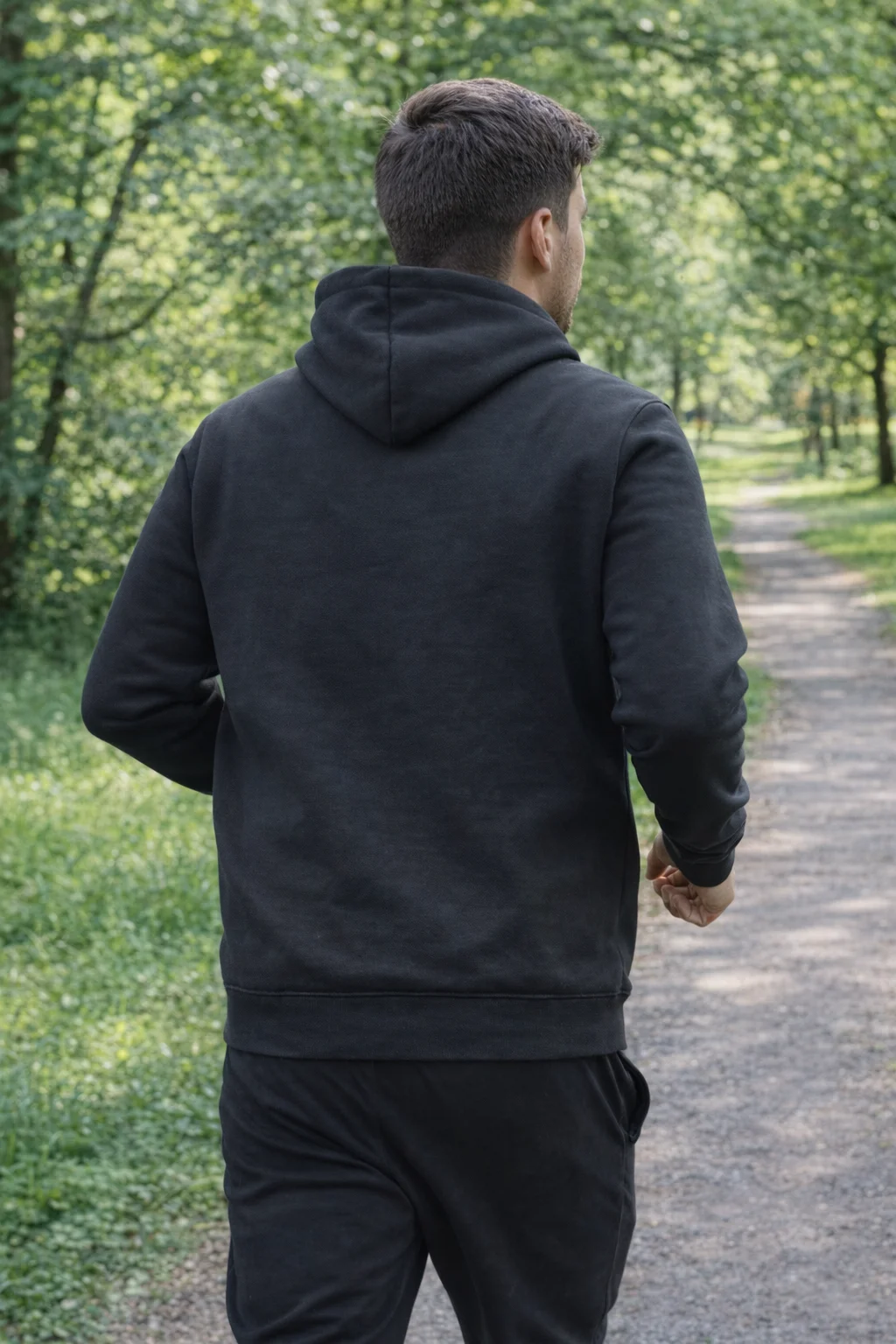 Man in a Jb's Branded Hoodie walks on a forest path, viewed from behind.