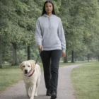 Woman in a Wo's Supply Hoodie walks a yellow Labrador retriever on a park path.