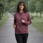 Curly-haired woman in Wo's Stencil Hoodie walks in a park with trees and a pathway.