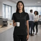 Woman wears Wo's Active Work Polo while holding a white mug in a modern office kitchen.