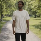 Man in Staple Tees walking on a sunlit park path surrounded by lush green trees.
