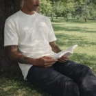 Man in Classic Tees reads a book while sitting against a tree in the park.