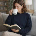 Woman on couch reading and sipping from a Supply Crewss mug.
