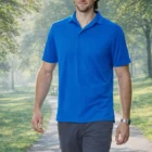 Man in a Men's Bamboo Charcoal Corporate Polo walks on a park path with sunlight and trees.