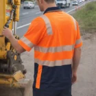 A man in a Biomotion Cooldry Safety Polo stands by roadwork equipment near a busy street.