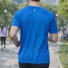 Man in Men's Extra Light Tee jogging in a park with people and trees in the background.