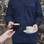 Barista in a Unisex Winter Closed Front Work Shirt serves coffee in a cozy café.