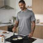 Man wearing Active Work Polos cooks two sunny-side-up eggs in a frying pan on the stove.