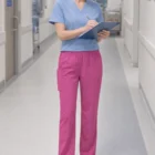 A nurse in Carevibe Unisex Pink V-Neck Scrub Pants writes on a clipboard in a hospital hall.