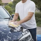 Wearing a Gildan Softstyle Adult Tri-Blend T-Shirt, this person washes a car outdoors.