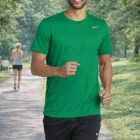 Man jogging in green Nike Legend Tee on park path, with trees and another person behind.