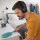 A man wears Anton Anc Headphones while dusting a white dresser in the bedroom.