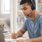 Man wearing Regent Meeting Headsets takes notes while working on his laptop at a desk.
