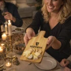 Smiling woman holds a Raffiel Bamboo Paddle Board with cheese and crackers at the table.
