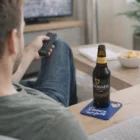 Man on couch with TV remote, Guinness, and Carusso Bottle Opener Coasters: Dance the Night Away.