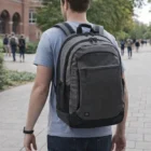 Person with a large gray Gateway Access Pack walks on a campus sidewalk in casual wear.