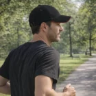 Man wearing Sand Peak Caps and black shirt jogging on a tree-lined park path.