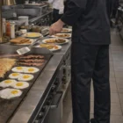 Wearing Cook Chef's Pants, plate eggs, bacon, and hash browns in a bustling kitchen.