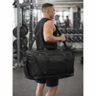 A man in gym wear carries a Stormtech Equinox 80 Duffle Bag in a weight room.