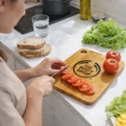 Slicing tomatoes on Large Logo Branded Bamboo Kitchen Boards with bread, lettuce, and water nearby.