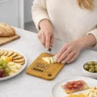 Person slicing cheese on a Small Promotional Wooden Cutting Board among snacks and appetizers.