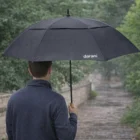 Person holding a Darani 58" Recycled Golf Umbrella stands on a rainy path.