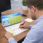 Man using a Desk Calendar to mark "Birthday!" with a red pen at his office desk.