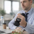 Man in office holds Dumb Bell Shapes next to salad and laptop.