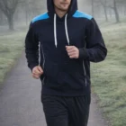 Man jogging in a park wearing Kz Adult's Kangaroo Pocket Contrast Hoodie and black pants.
