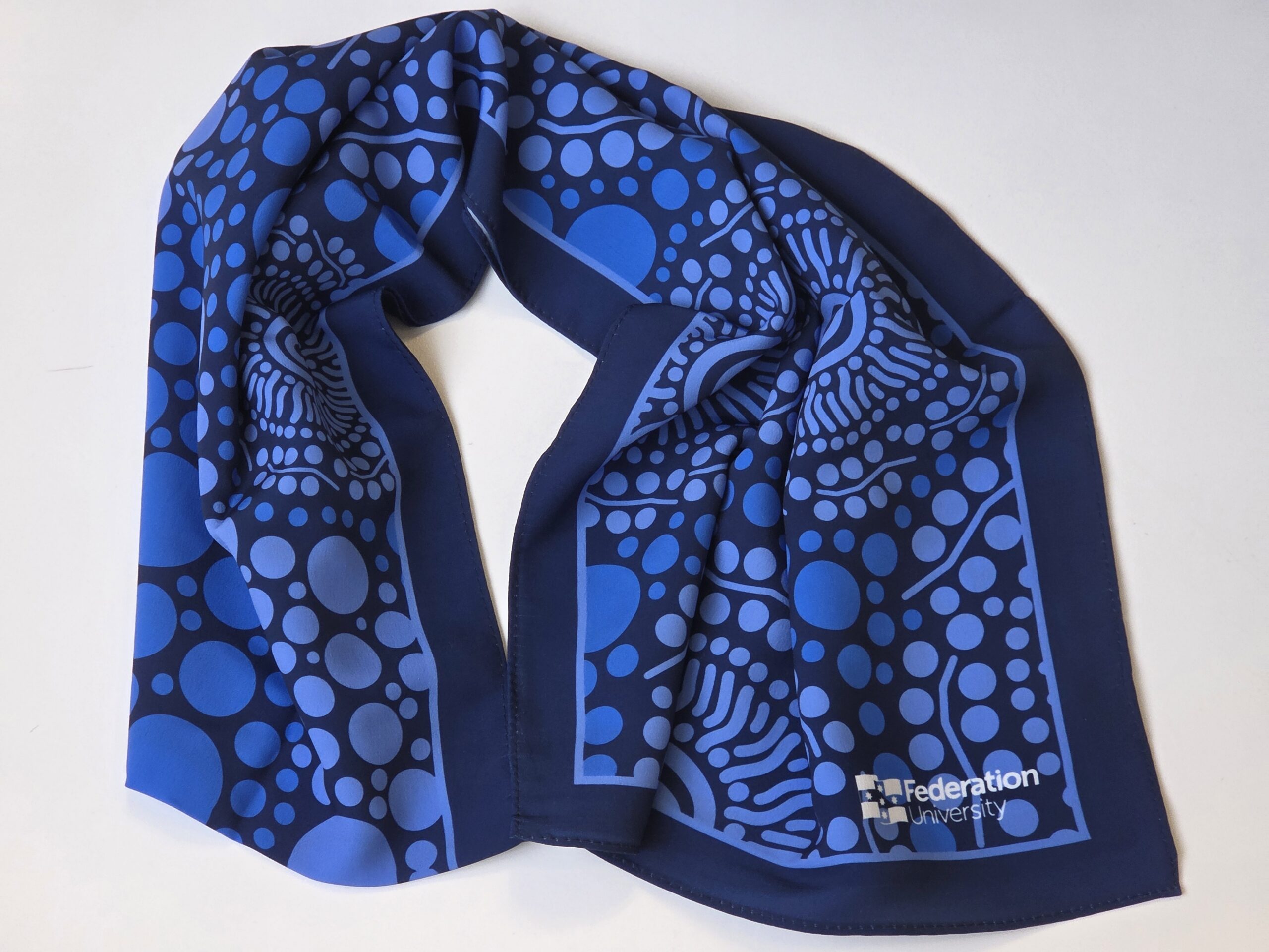 Blue scarf with abstract dot pattern and Ballarat’s Federation University logo in the corner.