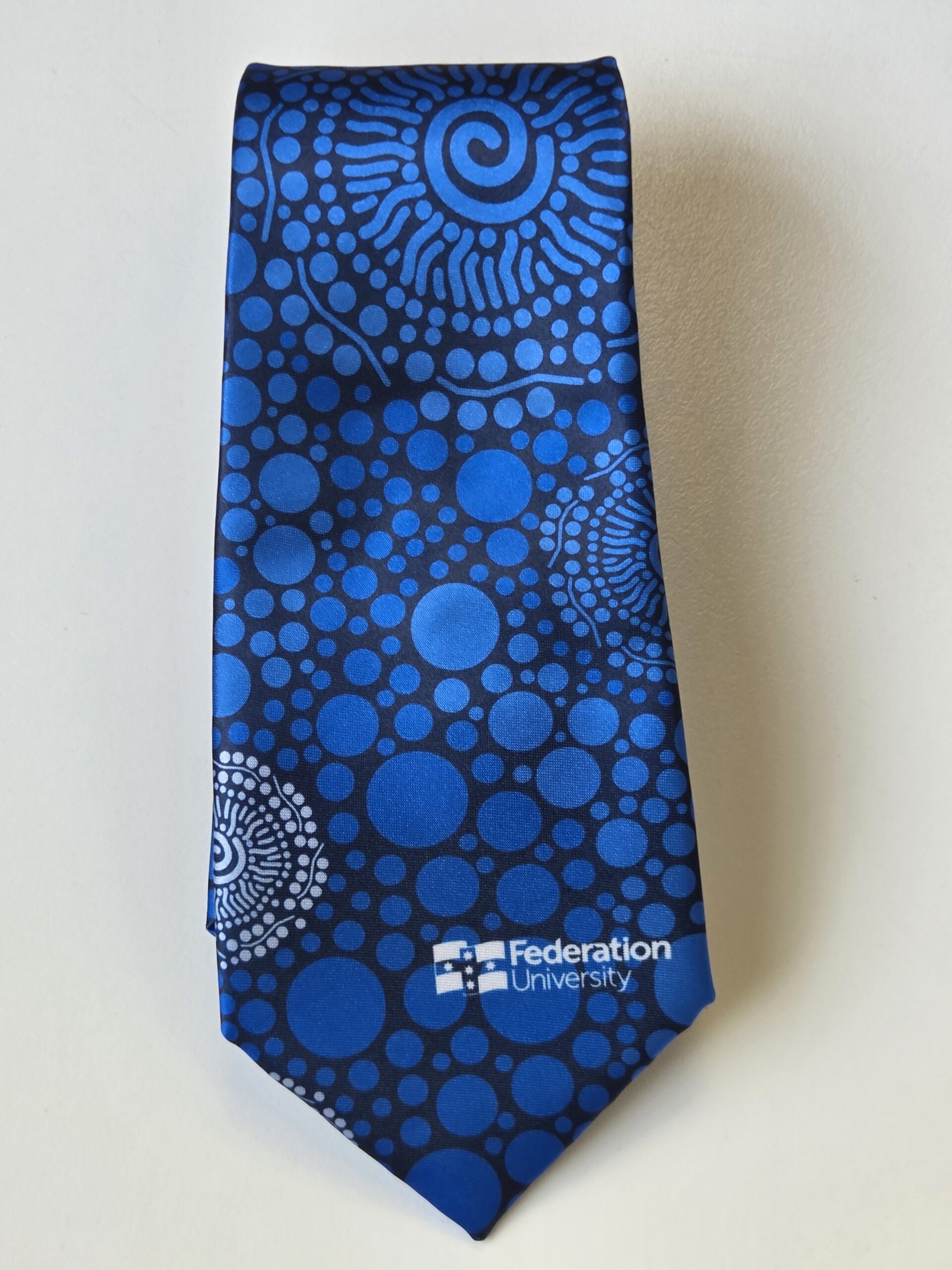 Blue tie with circular dot patterns and Federation University Ballarat logo in white at the bottom.