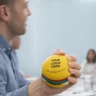 Person holding a Funky Stress Balls Hamburger with YOUR LOGO HERE printed on the front.