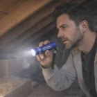 A man inspects an attic closely with the Beacon Mini Lightweight Torch.