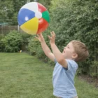 Young boy in yard reaching up to catch Beach Balls.