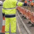 Worker in Tu Hi-Vis Safety Pants With 3M Tapes holds STOP sign and cone at roadwork site.