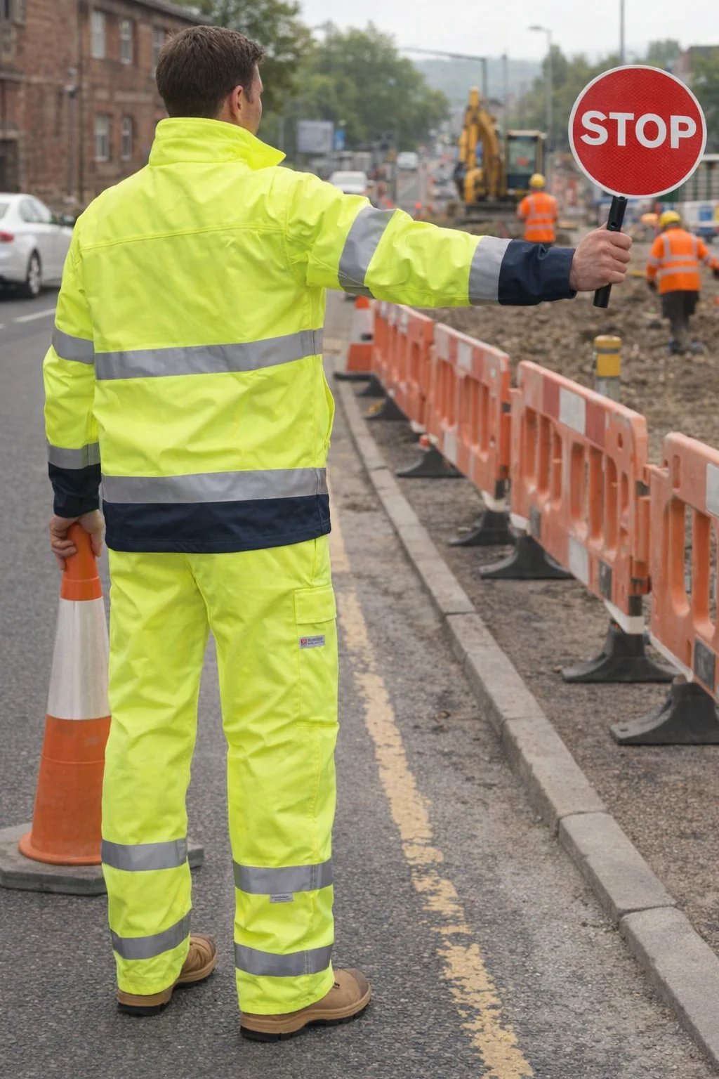 Worker in Tu Hi-Vis Safety Pants With 3M Tapes holds STOP sign and cone at roadwork site.